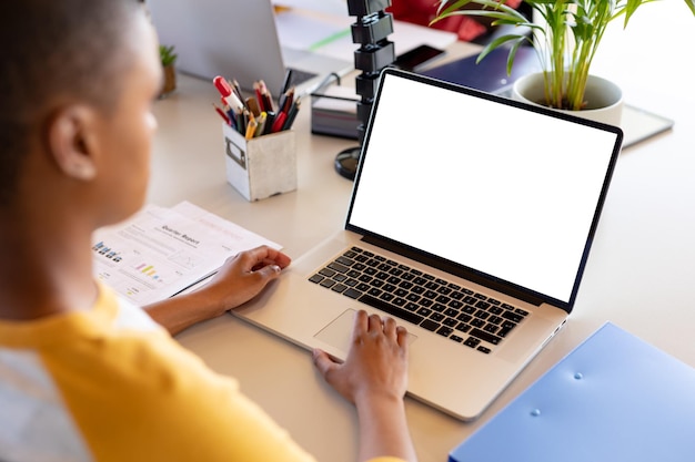 Mujer de negocios afroamericana en uso informal usando una computadora portátil con espacio para copiar en el escritorio de la oficina