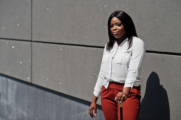 Mujer de negocios afroamericana vestida formalmente en blusa blanca y pantalón rojo con bastón a mano. Exitosa empresaria de piel oscura.