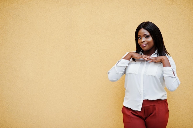 Mujer de negocios afroamericana vestida formalmente con blusa blanca y pantalones rojos aislados en fondo amarillo Exitosa mujer de negocios de piel oscura