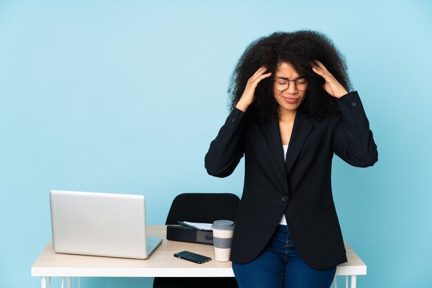 Mujer de negocios afroamericano que trabaja en su lugar de trabajo con dolor de cabeza