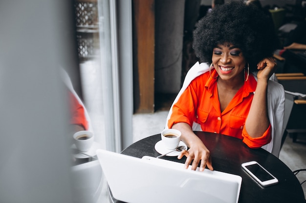 Mujer de negocios afroamericano en traje blanco trabajando en equipo portátil en un café