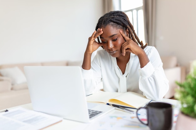 Foto mujer de negocios agotada que tiene dolor de cabeza en la oficina en casa mujer creativa afroamericana que trabaja en el escritorio de la oficina sintiéndose cansada mujer de negocios estresada que siente dolor en los ojos mientras trabaja demasiado