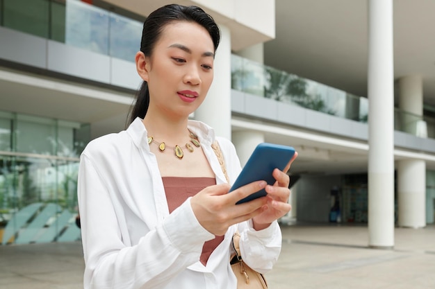 Mujer de negocios alegre leyendo mensajes de texto de su compañero de trabajo mientras está al aire libre