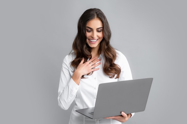 Mujer de negocios alegre de pie sobre una pared gris con computadora portátil