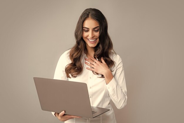 Mujer de negocios alegre de pie sobre una pared gris con computadora portátil