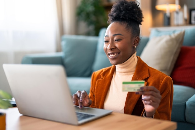 Mujer de negocios alegre con tarjeta de crédito y compras en línea a través de una computadora portátil en la oficina de su casa