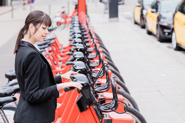 Mujer de negocios alquilando una bicicleta eléctrica compartida en las calles de la ciudad de camino al trabajo