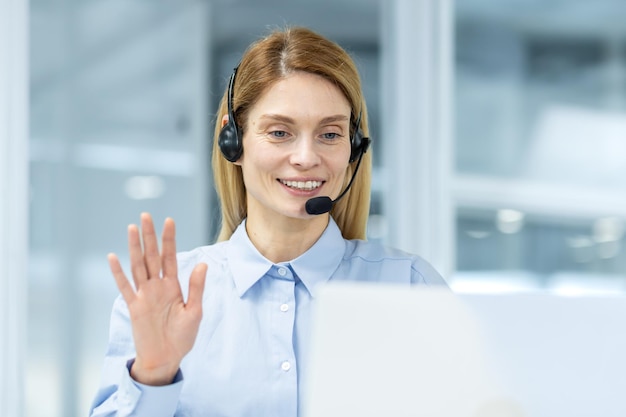 Una mujer de negocios amigable con auriculares haciendo un alegre gesto de saludo durante una videoconferencia