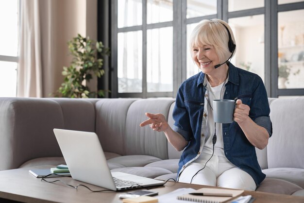 Mujer de negocios anciana con auriculares haciendo una conferencia telefónica en un centro de llamadas para ancianos.