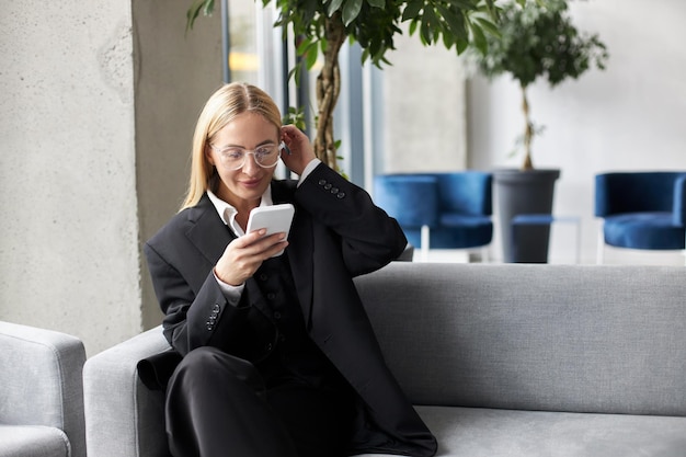 Mujer de negocios con anteojos elegantes sosteniendo un teléfono móvil revisando la comunicación por correo electrónico en línea