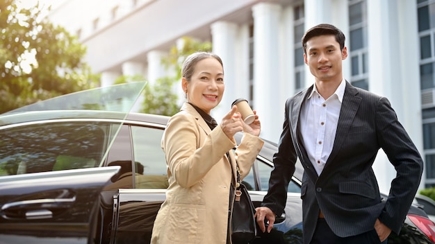 Mujer de negocios asiática anciana y hombre de negocios con traje formal de pie frente al auto