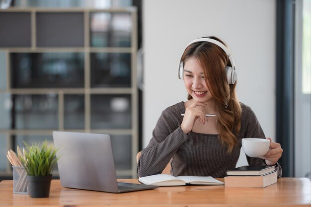 Mujer de negocios asiática con auriculares sentada y relajada sosteniendo una taza de café en la oficina