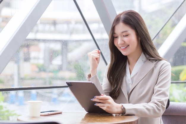 Mujer de negocios asiática con cabello largo en un traje color crema trabaja desde cualquier lugar fuera de la oficina