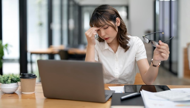 Mujer de negocios asiática cansada con dolor de cabeza en la oficina sintiéndose enferma en el espacio de copia de trabajo