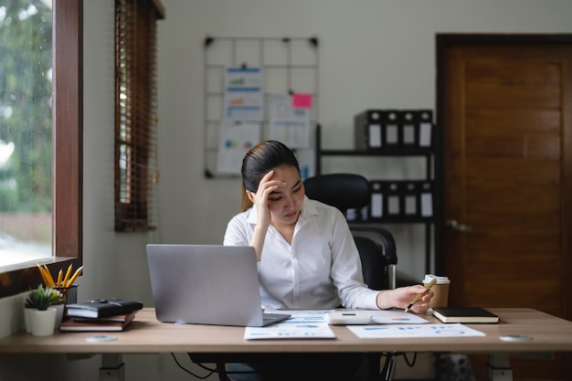 Mujer de negocios asiática cansada con dolor de cabeza en la oficina sintiéndose enferma en el trabajo