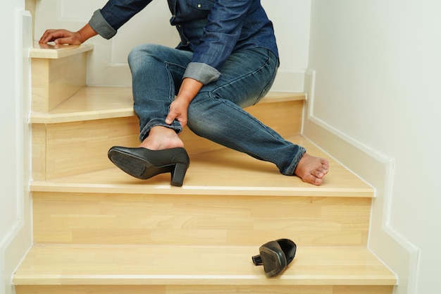 Mujer de negocios asiática dolor en el pie del tobillo con calambres en las piernas y caída por las escaleras porque las superficies resbaladizas en la oficina