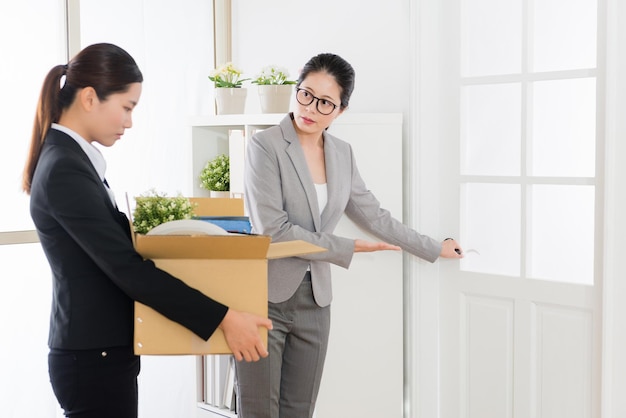 La mujer de negocios asiática es despedida por el jefe y el asistente la ayuda a abrir la puerta ya que llevaba muchas cosas en la mano.