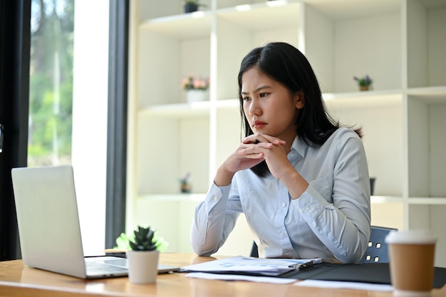 Una mujer de negocios asiática estresada está mirando la pantalla de su computadora portátil con una cara seria