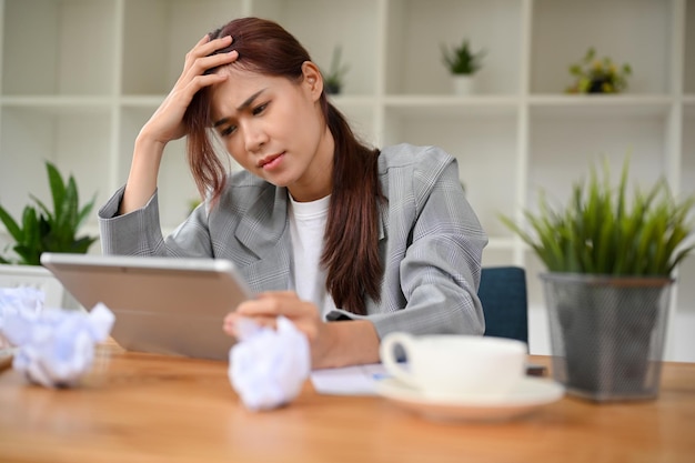 Mujer de negocios asiática estresada insatisfecha con su trabajo usando una tableta portátil