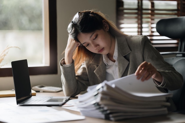 Una mujer de negocios asiática estresada se preocupa con muchos documentos en el escritorio de la oficina