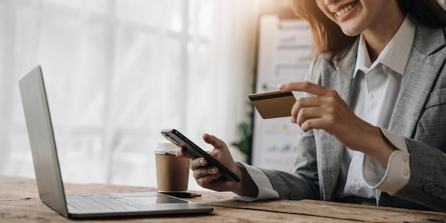 Mujer de negocios asiática feliz paga en línea usando el teléfono móvil en la oficina