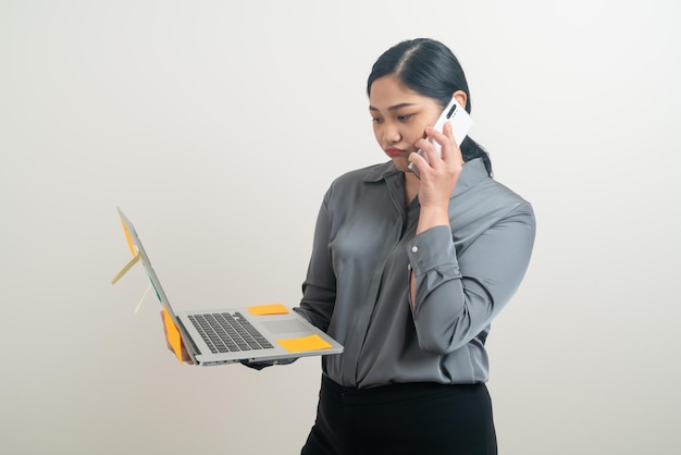 Mujer de negocios asiática hablando por teléfono con la mano que sostiene la computadora portátil