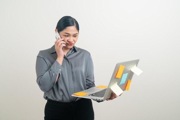 Mujer de negocios asiática hablando por teléfono con la mano que sostiene el portátil sobre fondo blanco.