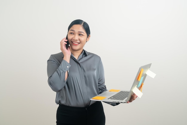 Mujer de negocios asiática hablando por teléfono con la mano que sostiene el portátil sobre fondo blanco.