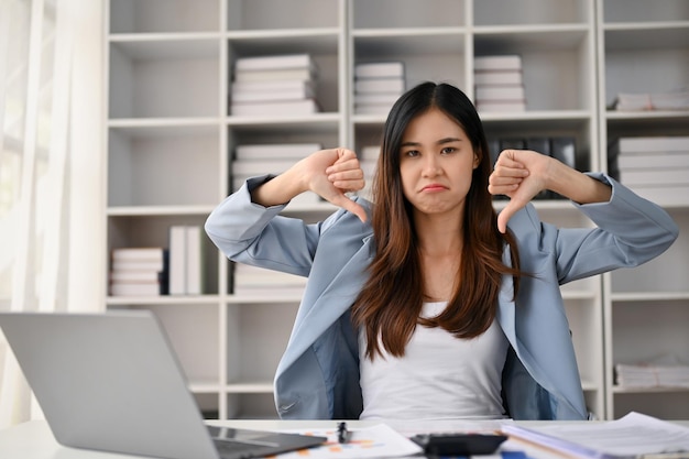 Mujer de negocios asiática insatisfecha y molesta mostrando los pulgares hacia abajo gesto de disgusto