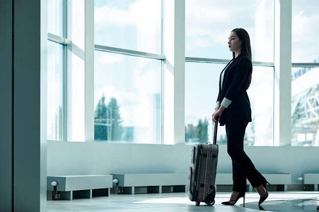 Mujer de negocios asiática joven en aeropuerto con bolsa de equipaje, esperando la salida