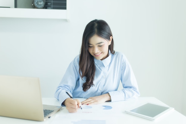 Mujer de negocios asiática joven que trabaja en el escritorio en oficina con los documentos y el ordenador portátil.