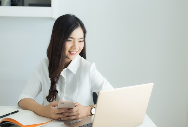 Mujer de negocios asiática joven que trabaja en su smartphone y computadora portátil en el lugar de trabajo.