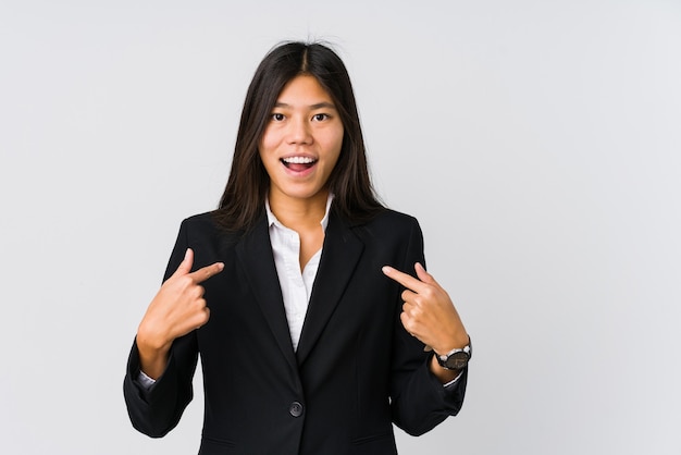 Mujer de negocios asiática joven sorprendida señalando con el dedo, sonriendo ampliamente.