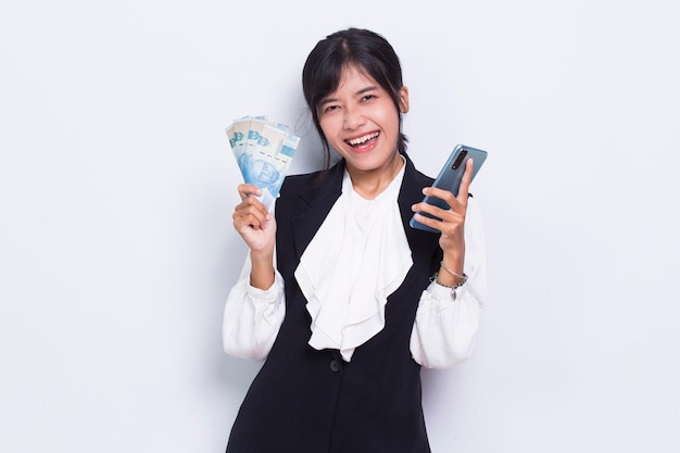 Mujer de negocios asiática mostrando dinero y sosteniendo teléfono móvil aislado sobre fondo blanco.