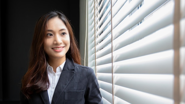 Mujer de negocios asiática profesional de pie sonriendo con confianza en la oficina