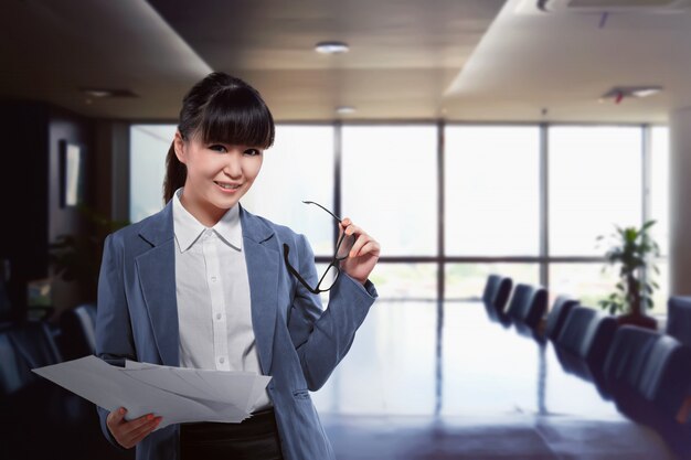 Mujer de negocios asiática que sostiene el papel y los vidrios