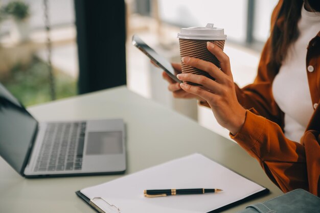 Foto mujer de negocios asiática que trabaja en una computadora portátil busca trabajo en línea freelance mirando y escribiendo en el cuaderno en la mesa estilo de vida de la mujer estudiando en línea