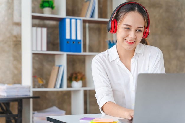 Mujer de negocios asiática que trabaja en una computadora portátil y usa auriculares estéreo para escuchar música trabajar de forma remota en vivo transmitiendo un concepto relajado