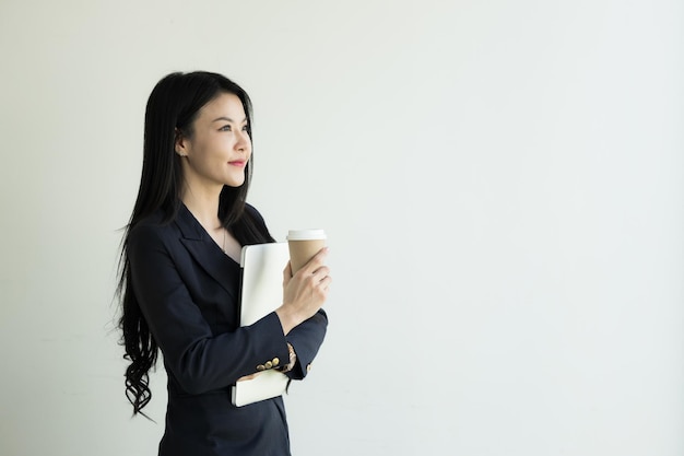 Mujer de negocios asiática que usa una computadora portátil mientras sostiene una taza de café Finanzas comerciales y empleo empresarias exitosas Mujer de negocios asiática agradable sonriente