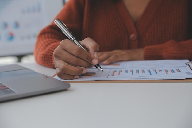 Mujer de negocios asiática que usa una computadora portátil y trabaja en la oficina con un documento de calculadora en el escritorio haciendo planificación analizando el concepto de análisis de finanzas de inversión del plan de negocios del informe financiero