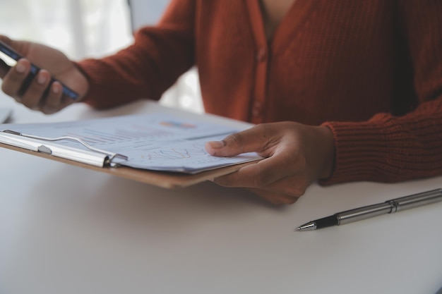 Mujer de negocios asiática que usa una computadora portátil y trabaja en la oficina con un documento de calculadora en el escritorio haciendo planificación analizando el concepto de análisis de finanzas de inversión del plan de negocios del informe financiero