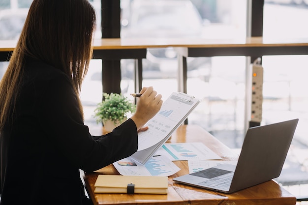 Mujer de negocios asiática que usa una computadora portátil y trabaja en la oficina con un documento de calculadora en el escritorio haciendo planificación analizando el concepto de análisis de finanzas de inversión del plan de negocios del informe financiero