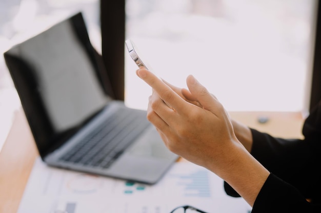 Mujer de negocios asiática que usa una computadora portátil y trabaja en la oficina con un documento de calculadora en el escritorio haciendo planificación analizando el concepto de análisis de finanzas de inversión del plan de negocios del informe financiero