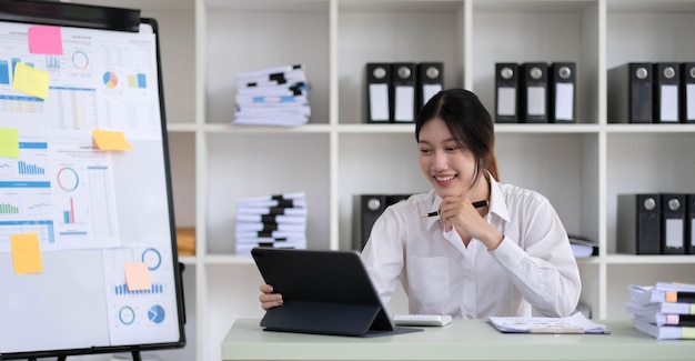 Mujer de negocios asiática que usa una computadora portátil y trabaja en la oficina con un documento de calculadora en el escritorio haciendo planificación analizando el concepto de análisis de finanzas de inversión del plan de negocios del informe financiero