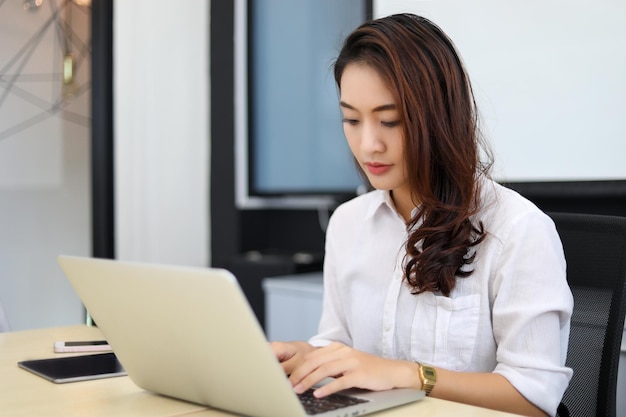 Mujer de negocios asiática que usa una computadora portátil para trabajar e investiga en Internet en su oficina