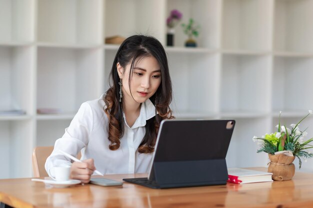 Mujer de negocios asiática sentada en la oficina sosteniendo un teléfono inteligente y una tableta colocados sobre la mesa