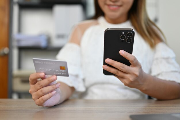 Foto mujer de negocios asiática sentada en su escritorio con una tarjeta de crédito y una foto recortada de su teléfono inteligente