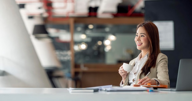 Mujer de negocios asiática sonriente feliz que trabaja en la computadora portátil en la oficina