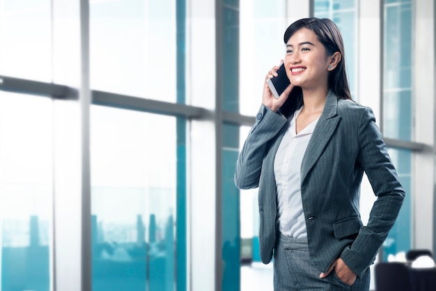 Mujer de negocios asiática sonriente que habla en su teléfono móvil