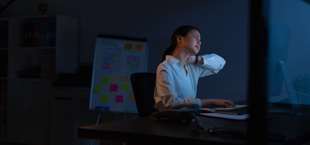 La mujer de negocios asiática tiene dolor de cuello porque usa la computadora y trabaja mucho tiempo por la noche.